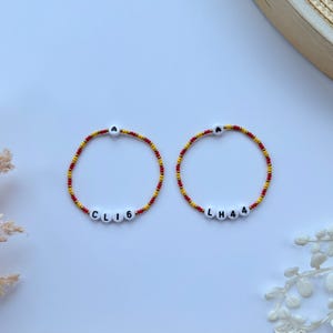 Peut inclure: Deux bracelets d'amitié avec des perles rouges et jaunes. Un bracelet épelle "CLIG" et l'autre "LHA4".