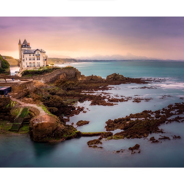 Biarritz Castle is located at the seafront in France, with beautiful mountains in the background and the sun setting down