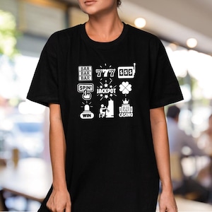 May include: Black t-shirt with a white graphic design of a slot machine with symbols like "777", "BAR", "$$$", "SPIN!" and "JACKPOT".