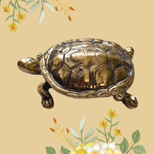 Pode incluir: Uma detalhada estatueta de tartaruga dourada com casco e membros texturizados. A tartaruga está posicionada sobre um fundo bege claro, com detalhes florais de flores amarelas e brancas e folhas verdes nos cantos.