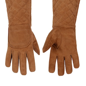 Könnte beinhalten: Ein Paar braune Wildlederhandschuhe mit roten gesteppten Manschetten. Die Handschuhe haben ein gestepptes Design und eine Tasche auf der Rückseite des linken Handschuhs.