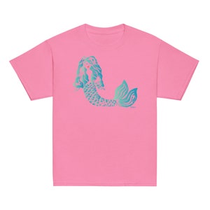 Puede incluir: Camiseta rosa con un gráfico de sirena azul turquesa. La sirena tiene el pelo largo y fluido y una cola escamosa.