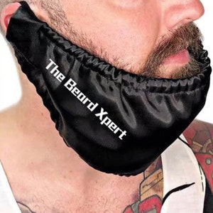 Puede incluir: Una cubierta de barba de satén negro con el texto "The Beard Xpert" en letras blancas.