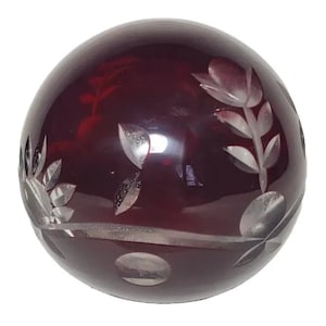 May include: A deep red glass ball with an etched floral design. The ball is smooth and shiny.