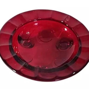 May include: A red glass dish with a scalloped edge and three small feet. The dish is made of clear glass with a red tint.