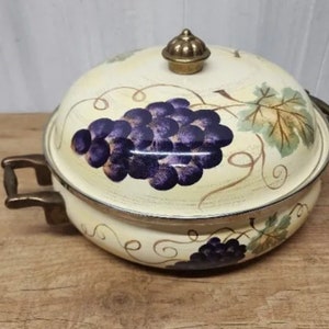 May include: A white enamel serving dish with a brass knob lid. The dish is decorated with a painted design of purple grapes and green leaves.