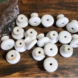 May include: A collection of white ceramic drawer pulls with a simple design. The pulls have a round base and a small knob on top.