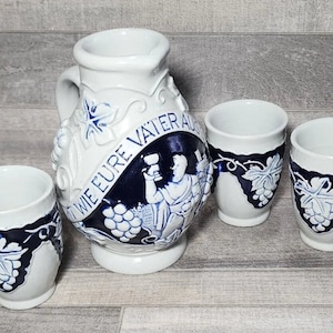 May include: A white ceramic pitcher with blue and white grapevine designs and the text "Wie eure Vater auch"  is surrounded by five matching ceramic cups.