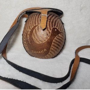 May include: A brown leather handbag with a woven design and a bird illustration. The bag has a black strap and says "Jamaica" on the front.