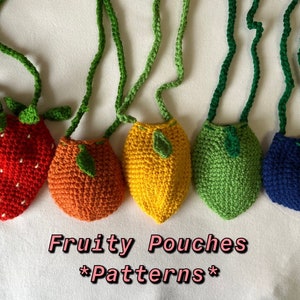 May include: Five crocheted fruit-shaped pouches with green straps. The pouches are shaped like a strawberry, orange, lemon, lime, and blueberry. The text "Fruity Pouches *Patterns*" is written below the pouches.