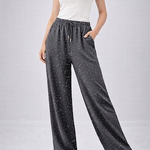 May include: A white sleeveless tank top paired with dark gray wide-leg trousers featuring a white speckled pattern, an elasticized waistband with a drawstring, and side pockets. The trousers have a loose, straight-leg fit and a smooth texture.