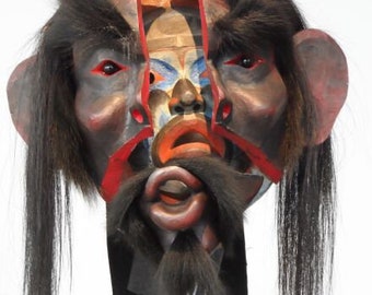 May include: A carved wooden mask with a split design, featuring a face with red accents, black hair, and a long black beard. The mask has a detailed, expressive face with red eyes and a painted design on the inner section.