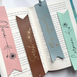 Può includere: Cinque segnalibri in pelle con lettere dorate e disegni floreali. I segnalibri sono di diversi colori: rosa, marrone, blu e verde. I nomi Olivia, Samantha, Sarah e Carmina sono scritti sui segnalibri.