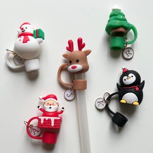 Könnte beinhalten: Fünf Weihnachts-Flaschenverschlüsse mit verschiedenen Figuren: ein Schneemann, ein Rentier, ein Weihnachtsbaum, der Weihnachtsmann und ein Pinguin. Jeder Verschluss hat einen Buchstaben-Anhänger.