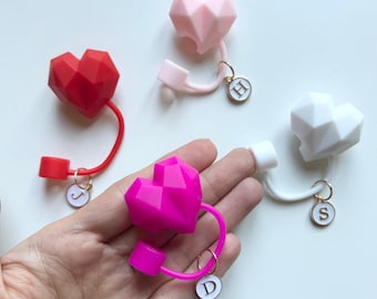 May include: Four geometric heart-shaped bottle stoppers in pink, red, white, and fuchsia with gold charms attached to each. The charms have the letters H, J, S, and D on them.