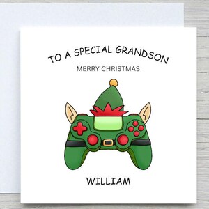 May include: A Christmas card with a white background and a green controller design. The controller is decorated with an elf hat and ears. The text reads "TO A SPECIAL GRANDSON, MERRY CHRISTMAS, WILLIAM."