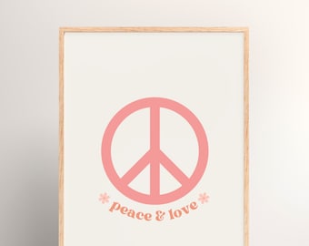 Op de afbeelding: Een ingelijste print met een roze vredesteken en de woorden "peace & love" in een retro lettertype. De achtergrond is lichtbeige en de lijst is van licht hout. Het ontwerp heeft een vintage uitstraling en straalt positiviteit uit.