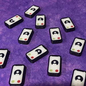 Puede incluir: Una colecci&oacute;n de cuentas rectangulares con una cara blanca, un icono de usuario negro, un c&iacute;rculo verde y un c&iacute;rculo rojo. Cada cuenta tiene un borde negro y un orificio para ensartar, dise&ntilde;adas como una interfaz de llamada telef&oacute;nica.