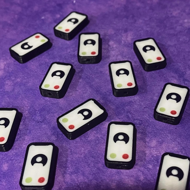 Puede incluir: Una colecci&oacute;n de cuentas rectangulares con una cara blanca, un icono de usuario negro, un c&iacute;rculo verde y un c&iacute;rculo rojo. Cada cuenta tiene un borde negro y un orificio para ensartar, dise&ntilde;adas como una interfaz de llamada telef&oacute;nica.
