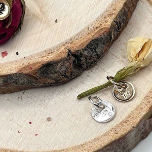 May include: Three pairs of silver and gold earrings with floral designs. The earrings are displayed on a wooden surface with dried flowers.