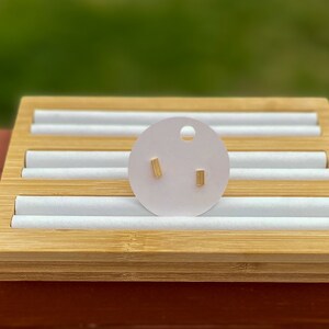 May include: A pair of gold bar stud earrings displayed on a white circular card with a small hole in the top. The card is sitting on a wooden display stand.