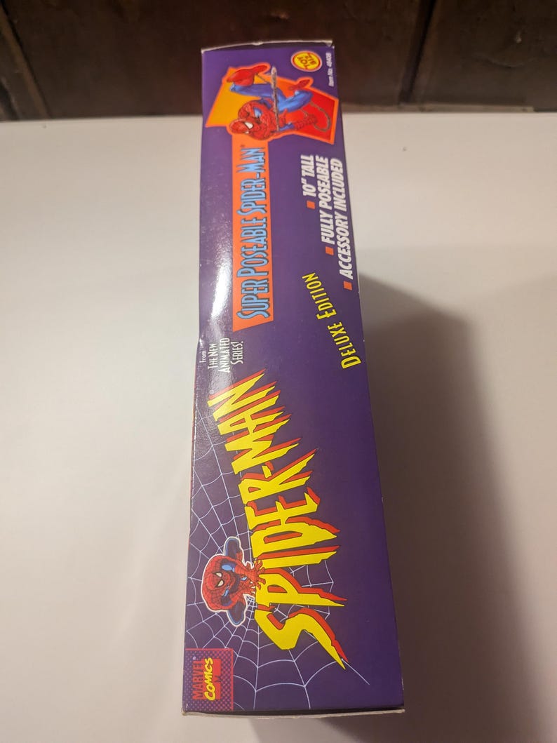 May include: A box for a 10-inch tall, fully poseable Spider-Man action figure. The box is purple with a spider web pattern and features a cartoon image of Spider-Man. The text on the box reads "Super Poseable Spider-Man Deluxe Edition".