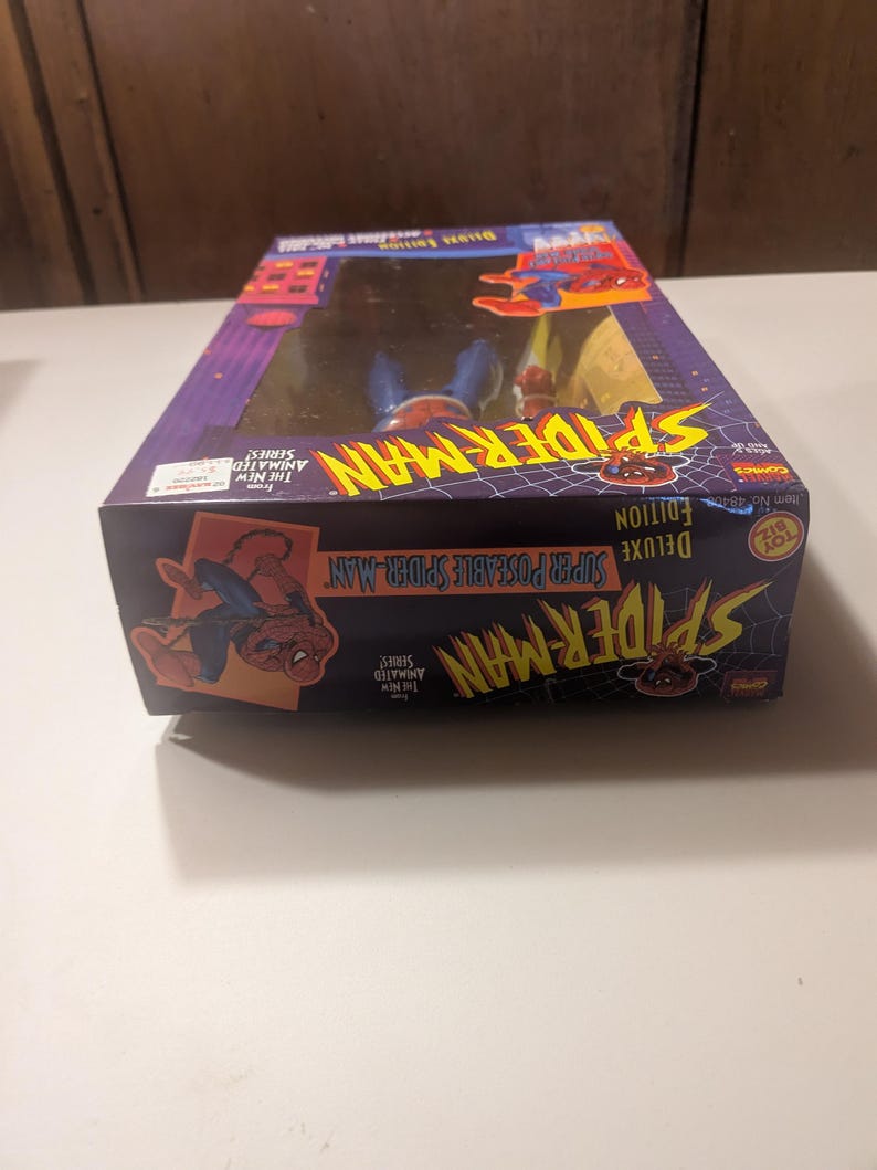 May include: A red and blue Spider-Man action figure in a box. The box is red, blue, and yellow with the words "Deluxe Edition Super Posable Spider-Man" on the front. The figure is from the "The New Animated Series" and is a "Toy Biz" product.
