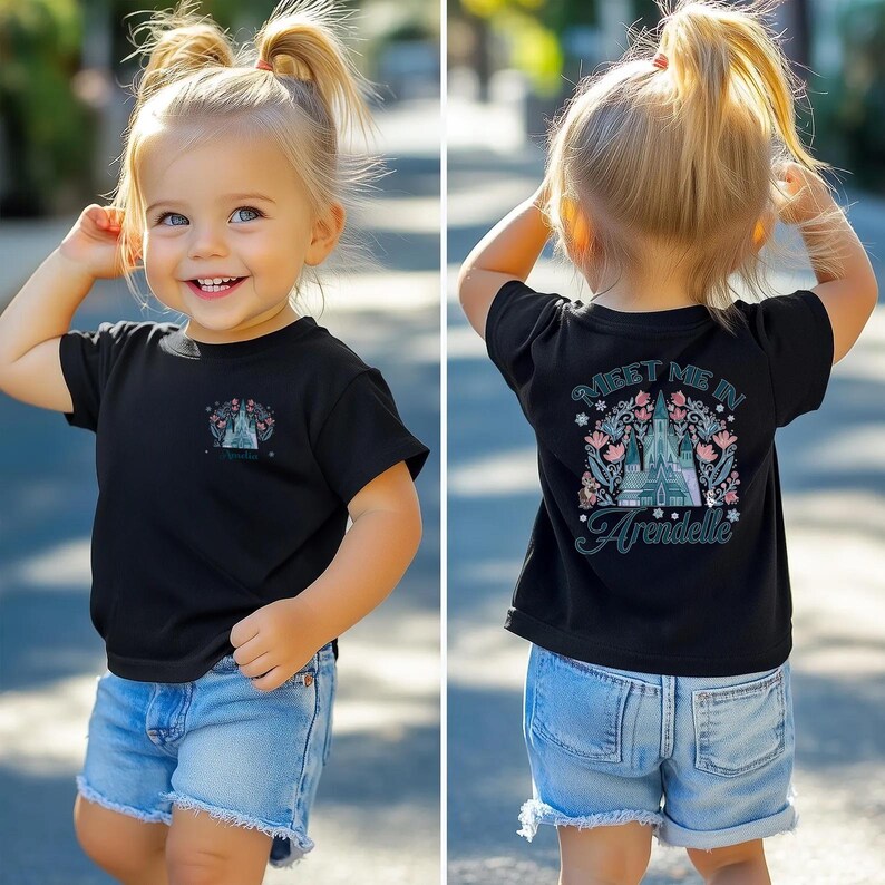 May include: Black t-shirt with a colorful graphic of a castle and the text "Meet Me In Arendelle". The shirt is worn by a young child, paired with denim shorts. The design includes floral and snowflake elements.