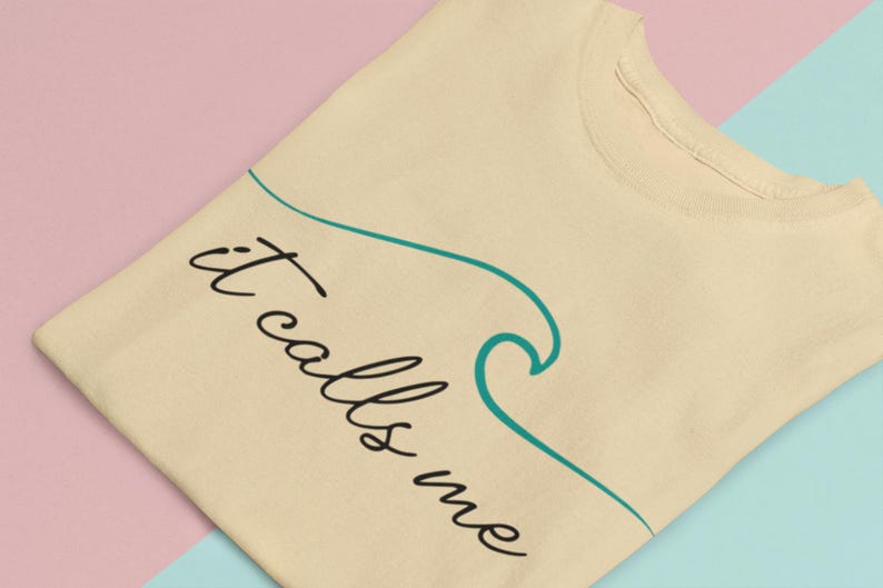 May include: A beige t-shirt with the text "it calls me" in black cursive writing. A teal blue wave graphic is drawn next to the text.