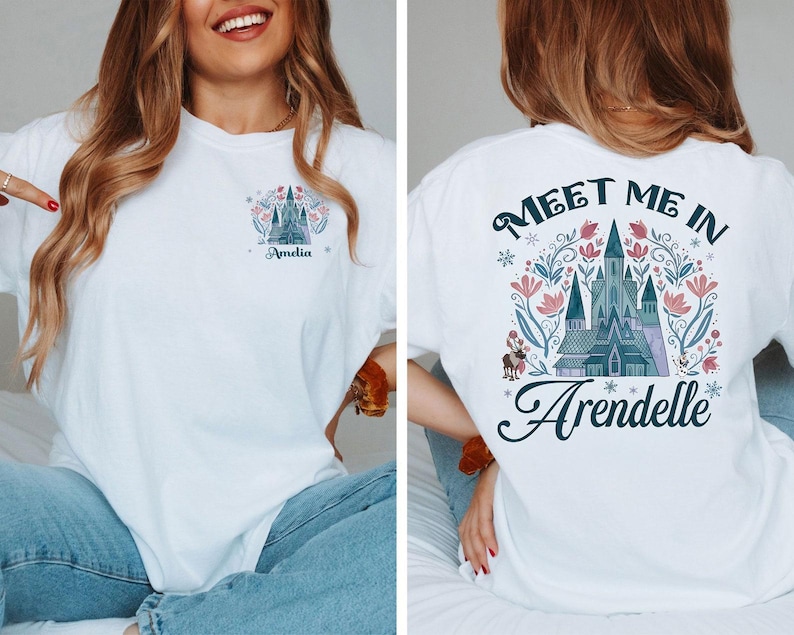 May include: White t-shirt featuring a castle design with the text "Meet Me In Arendelle" on the back. The front of the shirt has a smaller castle design and the name "Amelia". The design includes pink and blue floral elements.