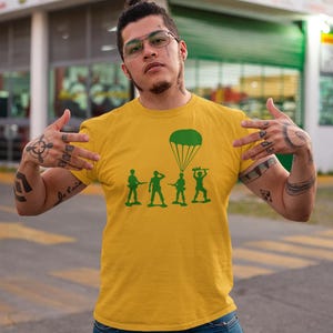Peut inclure: Un t-shirt jaune avec un motif vert de soldats de jouets en parachute. Les soldats tiennent des fusils et un parachute est au-dessus d'eux.