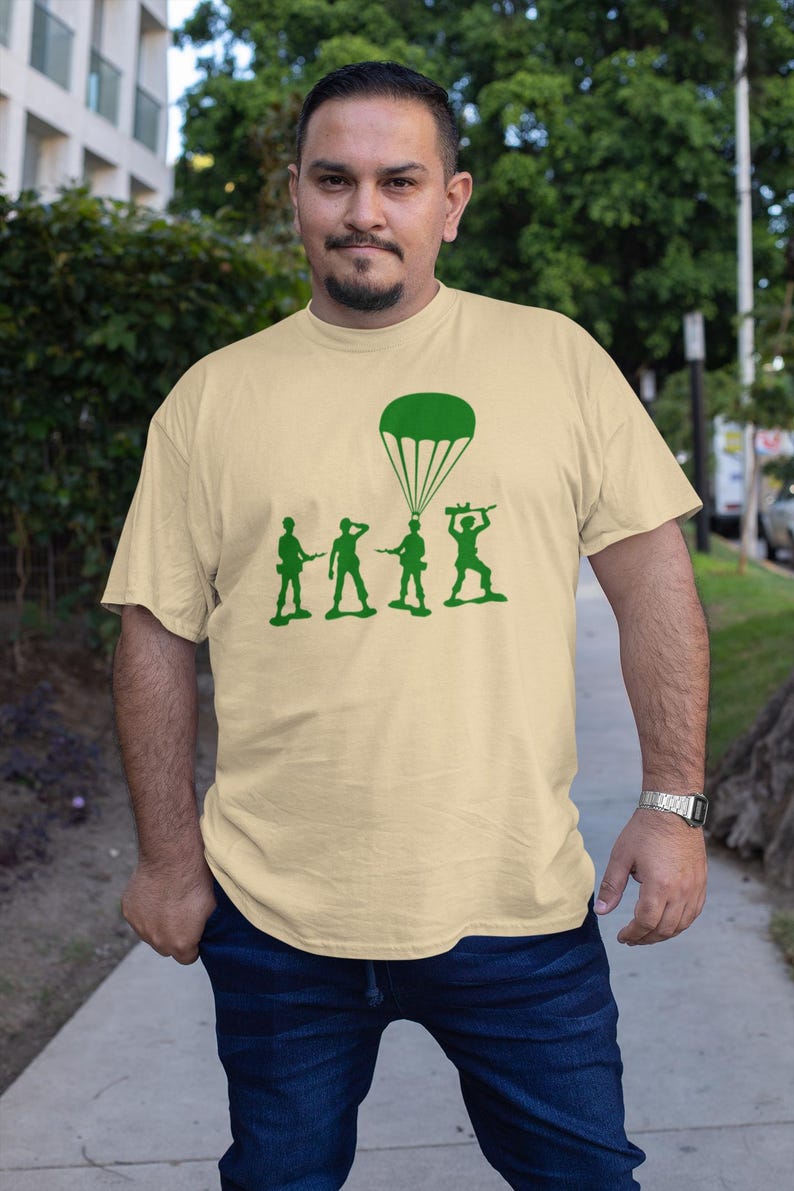 Peut inclure: Un t-shirt beige avec un motif vert d'un parachute et de quatre soldats en plastique. Les soldats sont en ligne, celui du fond tenant un parachute.