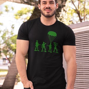 Peut inclure: Un t-shirt noir avec un motif vert de soldats en plastique, dont l'un est en parachute. Le motif comprend le texte "Army".