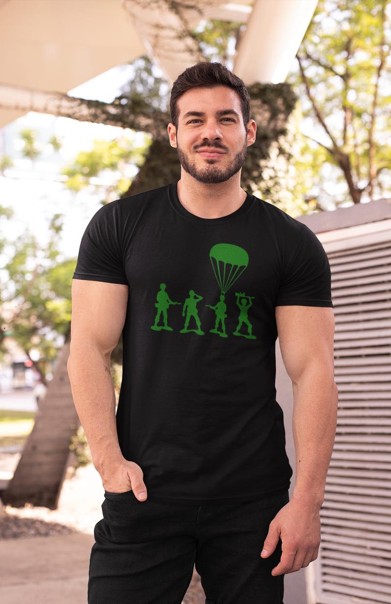Peut inclure: Un t-shirt noir avec un motif vert de soldats en plastique, dont l'un est en parachute. Le motif comprend le texte "Army".