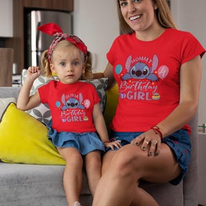 May include: Matching red t-shirts with a cartoon character and the words "Mommy Birthday Girl" and "Olivia Birthday Girl". The shirts are worn by a woman and a young girl, both wearing red headbands and denim skirts. The girl is sitting on a gray couch.