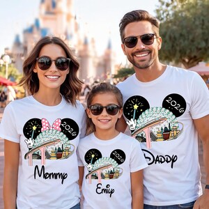 May include: White t-shirts featuring a colourful theme park graphic, a Mickey Mouse head, and the year 2026. The shirts are worn by a family, with the words "Mommy," "Emily," and "Daddy" printed on them.