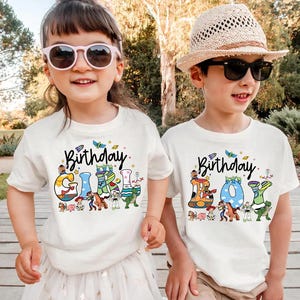May include: Two children wearing white t-shirts with the text "Birthday Girl" and "Birthday Boy". The shirts feature colorful cartoon graphics and the word "Birthday" in script. The girl wears pink sunglasses, and the boy wears a straw hat and black sunglasses.