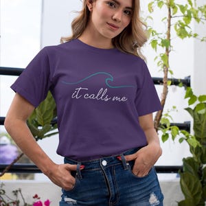 May include: A purple t-shirt with a teal wave graphic and the text "it calls me" in white.