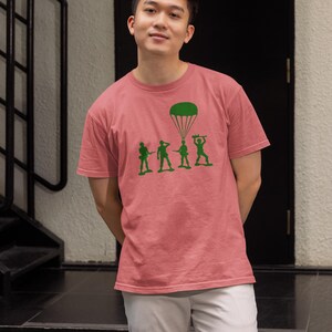 Peut inclure: Un homme portant un t-shirt rose avec un motif vert de soldats en jouet et un parachute. Le motif dit "Paratrooper".