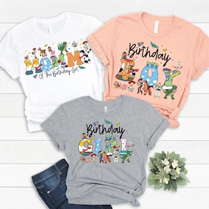 May include: Three t-shirts with colorful graphics. The white shirt says "Mommy of The Birthday Girl". The peach shirt says "Birthday Boy". The gray shirt says "Birthday Girl". All shirts have cartoon character designs.