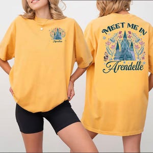 May include: Mustard yellow t-shirt with a castle graphic and the text "Meet Me In Arendelle" on the back. The front of the shirt has a smaller castle graphic and the name "Amelia".