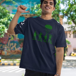 Peut inclure: Un t-shirt bleu marine avec un motif vert de soldats de jouets en parachute. Le motif repr&eacute;sente quatre soldats de jouets en ligne, avec un soldat tenant un parachute.
