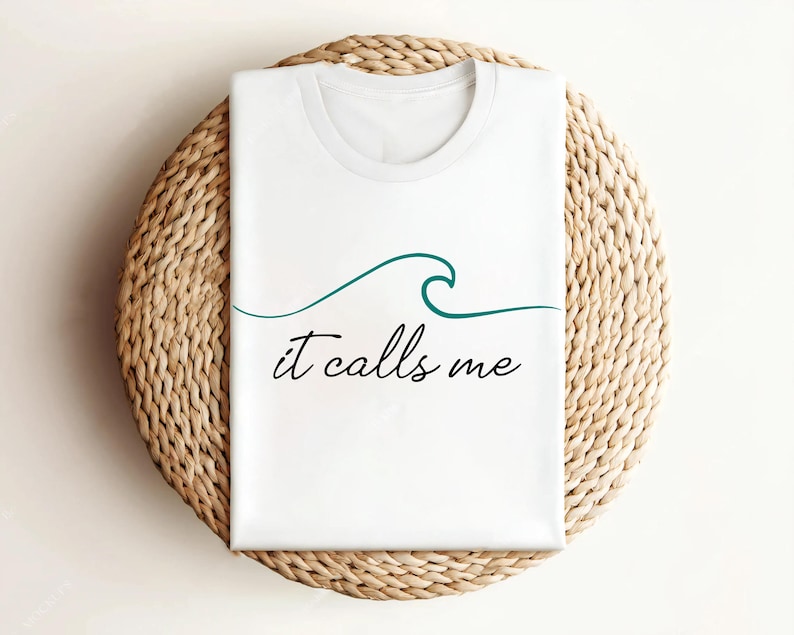 May include: White t-shirt with a teal wave graphic and the text "it calls me" in black.