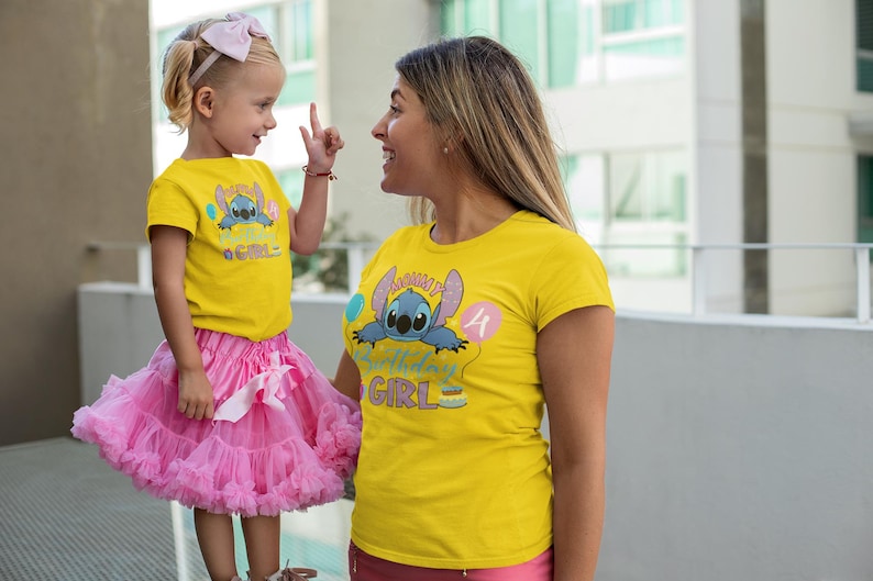 May include: Two people wearing matching yellow t-shirts with a cartoon character and the text "Birthday Girl". The child is wearing a pink tutu and a bow. The other person is wearing pink shorts.