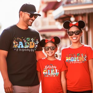 May include: Three people wearing matching t-shirts with birthday-themed designs. The father wears a black shirt that says "DADDY Of The Birthday Boy". The mother and daughter wear red shirts that say "MOM Of The Birthday Girl" and "Birthday GIRL".