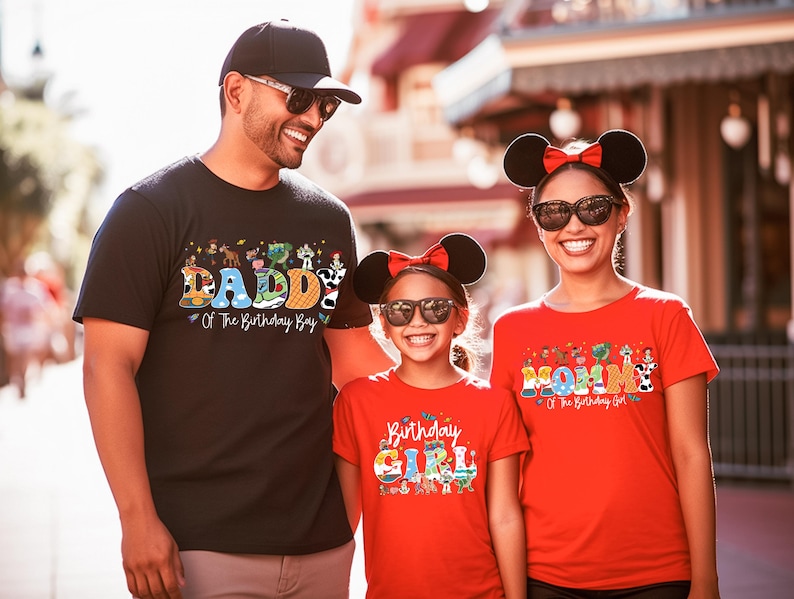 May include: Three people wearing matching t-shirts with birthday-themed designs. The father wears a black shirt that says "DADDY Of The Birthday Boy". The mother and daughter wear red shirts that say "MOM Of The Birthday Girl" and "Birthday GIRL".