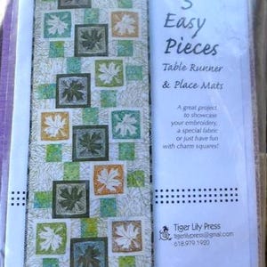 May include: A package featuring a table runner and place mats pattern. The design includes squares with leaf patterns in green, white, and orange. The text reads "3 Easy Pieces".