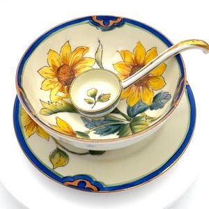 May include: A vintage ceramic serving set featuring a bowl, saucer, and small ladle. The set is decorated with yellow sunflowers, green leaves, and blue and orange trim. The ladle has a gold-colored handle.