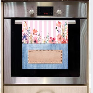 May include: A pink and white striped kitchen towel with a floral design and a blue denim pocket with a brown leather patch. The towel is hanging on an oven door.