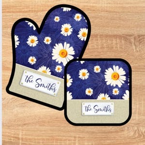 Puede incluir: Un juego de dos manoplas para horno de color azul y blanco con flores, con un borde de tela marrón y una etiqueta de nombre personalizada que dice "The Smiths".